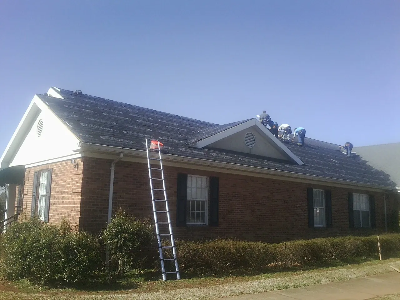 Crew tearing shingles off a brick ranch roof with a ladder set — Emergency Roof Repair work by our crew in Samaria