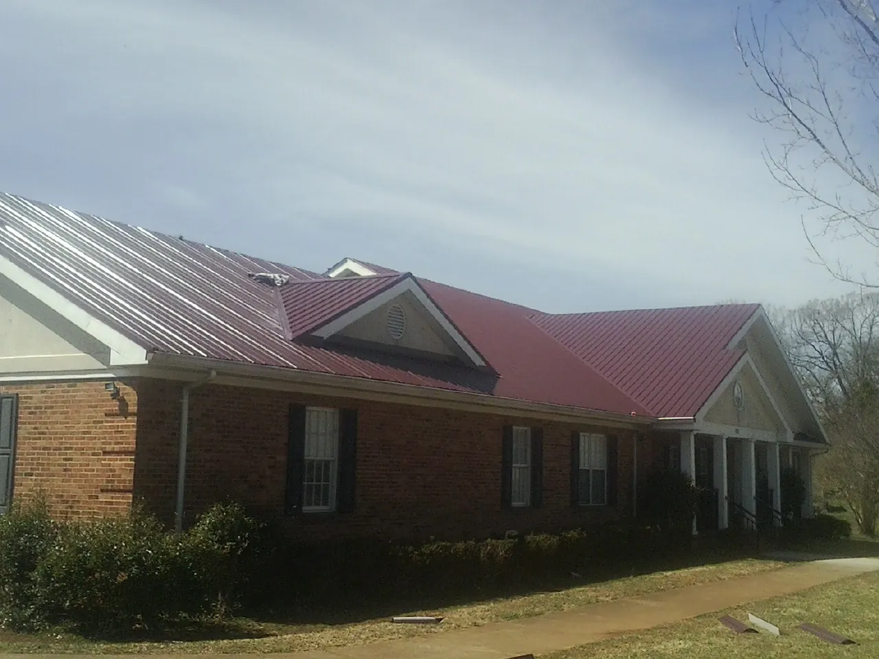 Red metal roof with gabled entries on a long brick building, from a Hail Damage Roof Repair job in Samaria