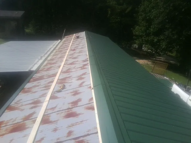 Old rusted panels beside newly installed green metal roofing — Wind Damage Roof Repair by Roofing Brothers in Samaria