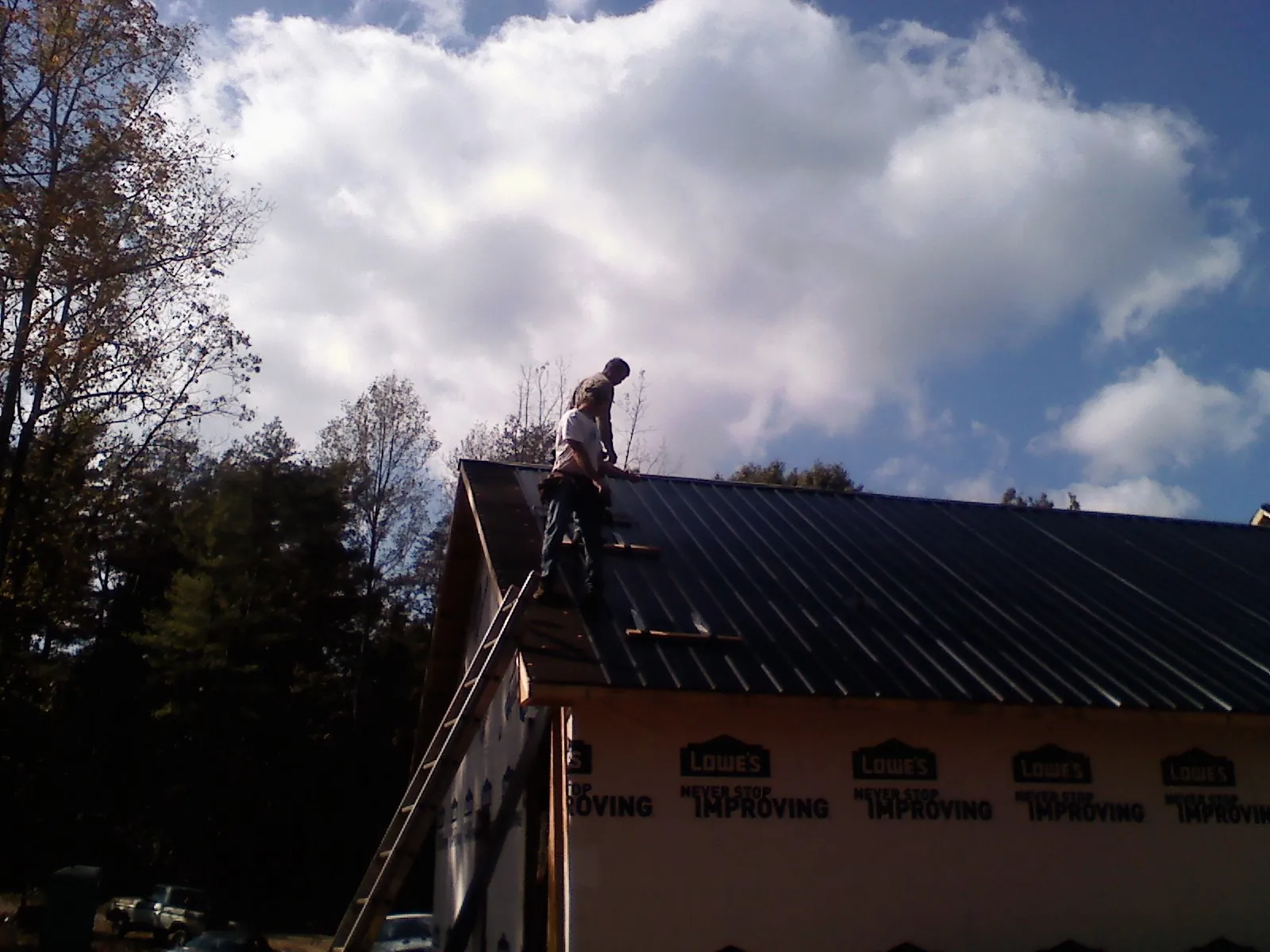 Roofer fastening dark metal panels high against a cloudy sky, from a Roof Inspection job in Samaria