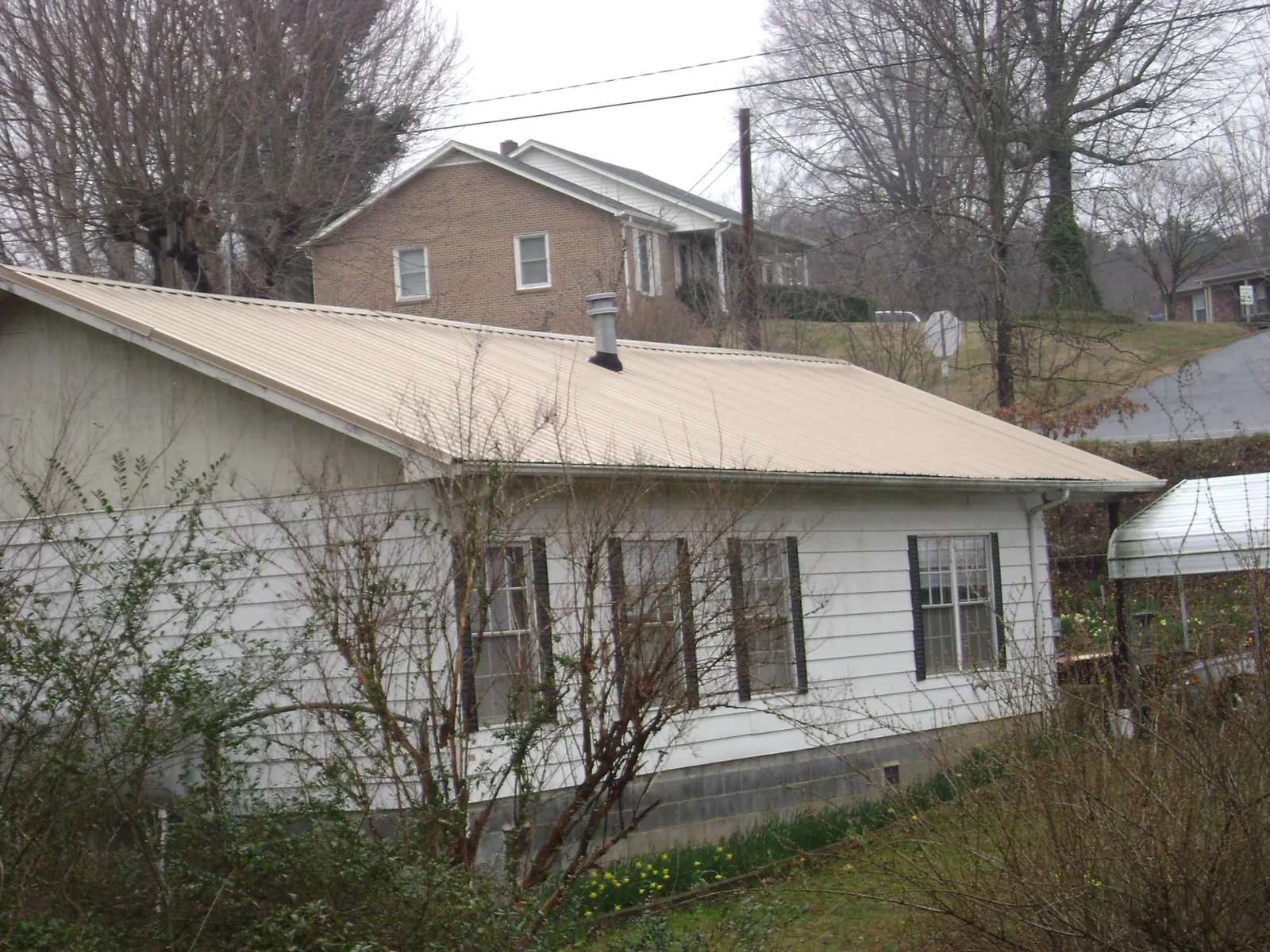 Tan metal roof on a white sided house set into a hillside — Commercial Roofing by Roofing Brothers in Samaria